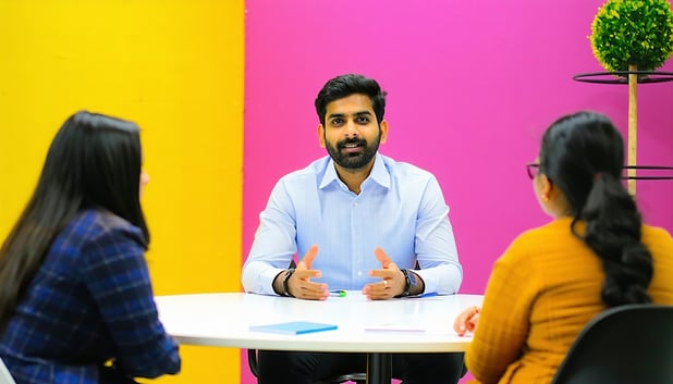 create an image where a confident Indian professional man is appearing for an interview in front of the interviewer across the table The interview room has vibrant wall and is aesthetic-4